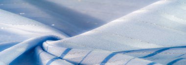 Zarif çizgileri olan bulanık mavi kumaş ve parlak röfleler güneş ışığı altında huzurlu bir akış yaratıyor. Yumuşak dokusu ve narin kıvrımları ışıldayan, barışçıl bir ortam oluşturuyor..