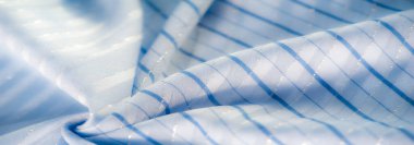 Bulanık açık mavi kumaş, yatay çizgiler ve ince parlaklıkla doğal ışık altında yavaşça akıyor. Yumuşak doku ve pürüzsüz yüzey zarif ve rahatlatıcı bir görsel yaratıyor..