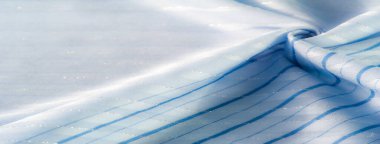 Bulanık mavi kumaş, yumuşak mavi çizgiler ve narin parıltılarla çizili. Güneş ışığı yumuşakça kıvrımları aydınlatır. Kumaşın pürüzsüz ve sakin dokusunu vurgular..