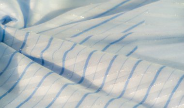 Akan organik çizgileri olan zarif mavi kumaştan bir bulanıklık. Kumaş ışığı nazikçe yakalar, yumuşak kıvrımlar ve yüzeyinde dans eden parıldayan çizgiler sergiler..