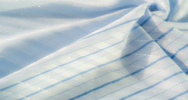 Bulanık mavi kumaş, yumuşak mavi çizgiler ve narin parıltılarla çizili. Güneş ışığı yumuşakça kıvrımları aydınlatır. Kumaşın pürüzsüz ve sakin dokusunu vurgular..