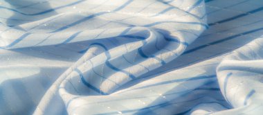 Bulanık açık mavi kumaş yumuşak, parıldayan bir dokusu ve doğal ışık altında zarifçe katlanmış ince çizgileri var. Parlayan kumaş, sanatsal tasarımlar için ideal bir görünüm sunuyor.