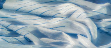 Işıltılı, bulanık mavi kumaş, ince çizgiler. Kumaş dokusu yumuşak ve akışkan görünüyor. Derinliği yansıtan bir şekilde, zarif arka planlar ve tasarımlar için ideal.