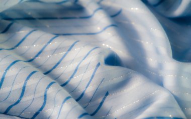 Yansıtıcı yüzeyleri ve ince çizgili deseni olan parlak mavi kumaş bulanıklığı. Yumuşak kıvrımlar, doğal ışık ve gölgeyle güçlendirilmiş zarif ve akıcı bir görüntü yaratır..