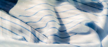 Açık mavi kumaştan bulanık, ince çizgili desenler yumuşak dalgalarda yavaşça akıyor. Işığın ve gölgenin narin parıltısı ve etkileşimi ruhani bir doku yaratır..