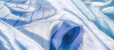 Yüzeyden yansıyan parıldayan ışıkla birlikte mavi kumaştan bulanık, narin kıvrımlı ve ince çizgili desenli yumuşak, akışkan bir görünüm yaratıyor..