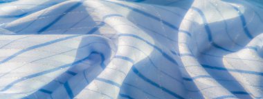 Dikey çizgileri olan yumuşak mavi kumaş bulanıklığı. Kumaştaki hafif oyun yumuşak bir parıltı ekler, zarif kıvrımlar ise gevşek ve akışkan bir doku oluşturur..