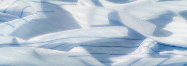 İnce çizgileri ve yansıtıcı iplikleri olan açık mavi kumaşın bulanık görüntüsü. Işık ve gölge oyunu yumuşak ve rahatlatıcı bir atmosfer yaratır. Sakinleştirici bir zemin ya da tekstil konsepti için mükemmeldir..