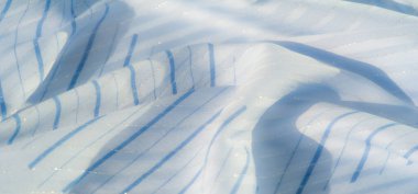 Açık mavi kumaş bulanıklığı, yatay çizgiler ve parlak detaylar. Kumaş pürüzsüz, yumuşak dokuları ve ışık yansımaları olan zarif akışkan şekiller yaratır..