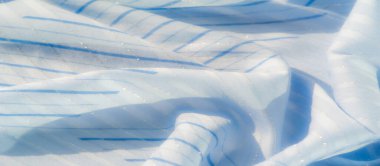 Açık mavi kumaş, dikey çizgiler ve parıldayan bir doku. Kumaş yumuşak bir şekilde akarak hafif ışık yansımalarıyla sakin, pürüzsüz ve havadar bir görünüm oluşturur..