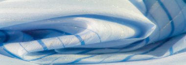 Bulanık soluk mavi kumaş, ince köşegen çizgileri ve parıldayan parıltıları var. Yumuşak kıvrımlar ve yumuşak ışık, kumaşın pürüzsüz ve hassas dokusunu vurgulayan sakin bir atmosfer yaratır..