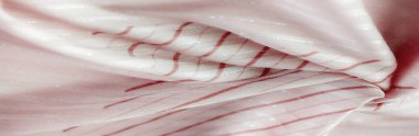 İnce, gümüş parıltılı çizgiler ve kalın kırmızı çizgiler içeren pembe kumaşın yakın plan görüntüsü. Kumaşın dokusu dalgalı, dinamik bir etki yaratıyor. İnce ve şık bir görüntü sunuyor..
