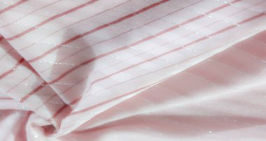 Pembe kumaşın detaylı bir görüntüsü yatay kırmızı çizgiler ve gümüş renkli aksanlar. Zarif kumaş hafifçe bükülmüş, gösterişli parlaklığını ve karmaşık tasarımını sergiliyor..