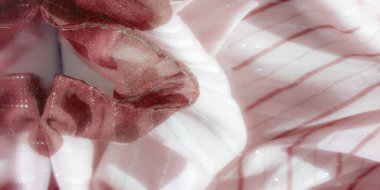 Kırmızı çizgiler ve gümüş parıldayan aksanlar içeren ince pembe kumaş bulanıklığı, kumaşın yumuşaklığını ve yansıtıcı özelliklerini arttıran karmaşık şekiller içinde katlanmış..