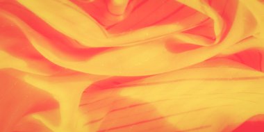 Yumuşak kıvrımlı ve çapraz desenli bulanık sarı-turuncu kumaş. Kumaş renklerin ve dokuların dinamik bir kombinasyonunu sergiliyor. Sıcak ışık pürüzsüz yüzeyinden yansıyor..