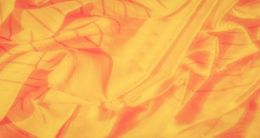 Bulanık sarı ve turuncu kumaşlar ince çapraz çizgiler ve kıvrımlar. Pürüzsüz, parlak yüzey soyut bir şablon oluşturur, ışık ve dokuma sanatsal bir oyun yaratır..