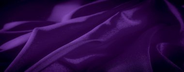 Bulanık mor saten kumaş kıvrımları hafif ışık yansımalarıyla maddenin zenginliğini ve derinliğini vurgulayan yumuşak, pırıl pırıl bir doku yaratır.