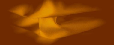 Bulanık turuncu kumaş kıvrımları, hafif ışık değişimleriyle maddenin yumuşak dokusunu geliştiren bir akış etkisi yaratır. Yumuşak eğriler bileşime derinlik ve sıcaklık ekler.