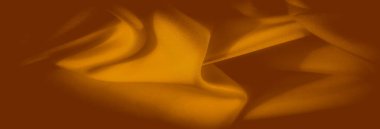 Görüntü, turuncu kumaş üzerine yumuşak bir odak, ince kıvrımlarını ve dokusunu ortaya çıkarıyor. Işık kumaşların yüzeyinde hareket eden sıcak ve davetkar bir desen oluşturuyor..