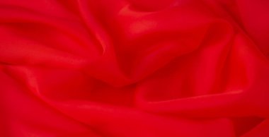 Yumuşak, nazik kıvrımları ve pürüzsüz dokuyu gösteren, lüks ve davetkar bir tekstil arka planı yaratan kırmızı kumaşın bulanık görüntüsü..