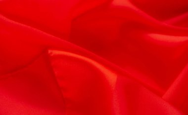 Yumuşak kıvrımlar ve pürüzsüz doku gösteren canlı kırmızı kumaş bulanıklığı. Yumuşak kıvrım, kumaşların ipeksi parıltısını vurgulayan bir derinlik ve sıcaklık hissi yaratır.