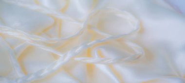 Yumuşak kıvrımlı ve örgülü iplikçikli beyaz kumaşın bulanık görüntüsü. İpeksi dokusu yumuşak ışığı yansıtıyor, sakin ve zarif bir atmosfer yaratıyor..