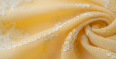 Görüntü, kıvrımlı beyaz işlemeli sarı kumaş karmaşık ve hassas bir tasarım yaratır. Kumaşın pürüzsüz kıvrımları yumuşak dokusunu ve sanatsal çekiciliğini vurgular.