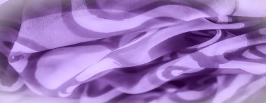Yüzeyinde ışık ve gölge oynayan yumuşak mor bir kumaşın bulanıklığı. Nazik kıvrımlar ve kıvrımlarla görsel dinamik ve soyut bir desen oluşturuyor..