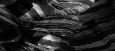 Katlanmış, parıldayan siyah kumaşı bulanıklaştırarak ışığın altında büyüleyici bir desen oluşturuyor. Lüks dokusunu vurguluyor. Parıltı derinlik ve incelik ekler..