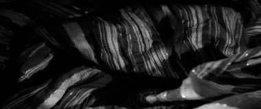 Katlanmış, parıldayan siyah kumaşı bulanıklaştırarak ışığın altında büyüleyici bir desen oluşturuyor. Lüks dokusunu vurguluyor. Parıltı derinlik ve incelik ekler..