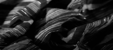 Örülmüş siyah kumaş yumuşak kıvrımlar ve parlak bir yüzey sergiliyor. Işığı ince bir şekilde yansıtıyor. Bu lüks tekstil her tasarıma biraz cazibe katar..