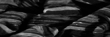 Bulanık, ince siyah kumaş. Karmaşık dikey çizgileri var. Parlak bir doku yaratıyor. Malzemenin yumuşak kıvrımları ışığa derinlik ve ince yansımalar ekler..