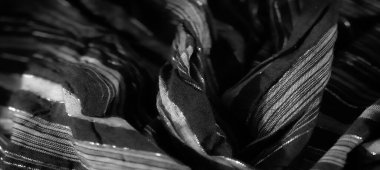 Görüntü, parlak çizgili sofistike siyah kumaş. Kumaşın nazik kıvrımları zarif bir ışık oyunu yaratıyor. Karmaşık desenleri vurguluyor ve lüks bir doku ekliyor..