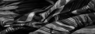 Işığı yansıtan karmaşık dokuma desenleri olan, parlak siyah kumaşın bulanık yakın çekimi, kumaşın pırıl pırıl ve lüks görünümünü arttırır..