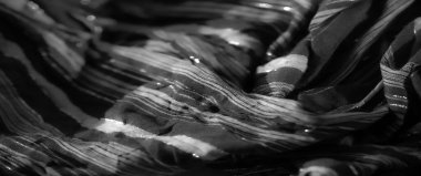 Işığı yansıtan karmaşık dokuma desenleri olan, parlak siyah kumaşın bulanık yakın çekimi, kumaşın pırıl pırıl ve lüks görünümünü arttırır..