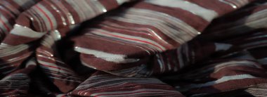 Görüntü. Kahverengi kumaş, beyaz ve kırmızı çizgiler ve parıldayan metalik iplikler yumuşak kıvrımlar ve yansıtıcı iplikler zarif tasarımını vurgulayarak lüks ve parlak bir doku yaratır.