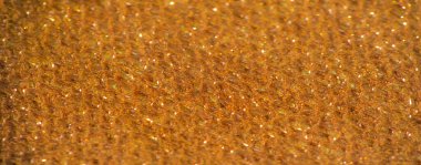 Işıldayan iplikler ve parlak gölgelerle bronz kumaşın bulanık yakın çekimi. Materyalin yumuşak kıvrımları ışığı yakalıyor, varlıklı ve sofistike bir görünüm yaratıyor..