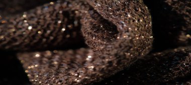 Katlanmış metalik desenli, parlak ışıklı bir kumaşın bulanıklığı. Ayrıntılı dokuma ışığı yansıtır, maddeye derinlik ve ışıltı ekler, onu iç tasarım için ideal kılar.