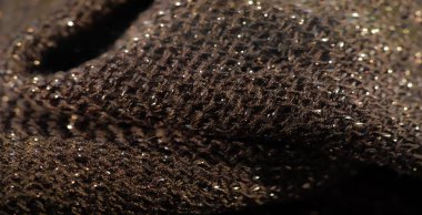 Metalik ipliklerle birbirine karışmış koyu dokulu bir kumaş bulanıklığı. Işığı yüzeyine yansıtıyor. Işıldayan dokuma, dinamik ve ışıltılı bir desen oluşturur.