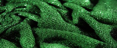 Karmaşık parlak dokusu olan yeşil kumaştan bulanık, düşük ışık altında hafif ve parıltılı, üst düzey moda tasarımı için mükemmel görsel dinamik bir tekstil sahnesi yaratıyor..