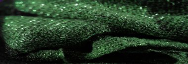 Pırıl pırıl parlayan yeşil kumaşın bulanık görüntüsü ve detaylı doku. Işıldayan yüzey ışığı yansıtır, dokuma karmaşıklığını ve canlı rengini gösterir..