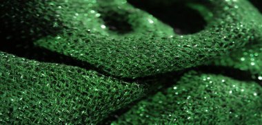 Parlak bir dokusu ve karmaşık dokuması olan yeşil parıltılı kumaşın bulanık görüntüsü. Parlak, parlak bir tekstil etkisi yaratmak için ışık yansıtan bir madde..