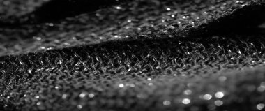 Parlayan yansımaları ve karmaşık dokuları olan bulanık kumaş. Işık, siyah dokuma yüzeyini yakalıyor ve kumaşların kıvrımlarını vurgulayan ışıltılı bir etki yaratıyor..