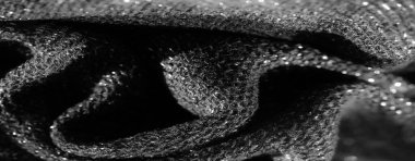 Karanlık, desenli bir kumaşın yakın plan görüntüsü parıldayan bir yüzey ve ince yansıtıcı detaylar sergiliyor, karmaşık dokumasını aydınlatıyor. Malzemenin ince kıvrımları derinlik ekler.