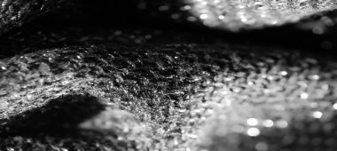 Parlak dokuması olan siyah kumaşın bulanık görüntüsü. Karmaşık dokusu ışığı yansıtır. Parıldayan bir parıltı yaratır. Bu parıltı maddenin yüzeyinin derinliğini ve detaylarını arttırır ve katlanır..