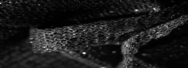 Siyah parıldayan kumaşın detaylı bir makro görüntüsü. Karmaşık dokumayı ve ışıkta parlayan yansıtıcı elementleri vurguluyor. Doku zengin ve lüks.