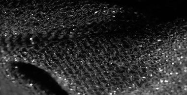 Siyah parıldayan kumaşın detaylı bir makro görüntüsü. Karmaşık dokumayı ve ışıkta parlayan yansıtıcı elementleri vurguluyor. Doku zengin ve lüks.