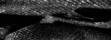 Siyah parıldayan kumaşın detaylı bir makro görüntüsü. Karmaşık dokumayı ve ışıkta parlayan yansıtıcı elementleri vurguluyor. Doku zengin ve lüks.