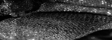 Görüntü, siyah desenli kumaşın parlak detaylarını yakından yakalar. Maddenin dokuması ışığı yansıtır, ince kıvrımlarla derinliği arttırır.