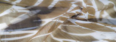 Görüntü, soyut beyaz yaprak benzeri tasarımları olan açık kahverengi bir kumaş. Kumaşlar ona organik bir akış sağlıyor, karmaşık ve dokulu bir görünüm yaratıyor..